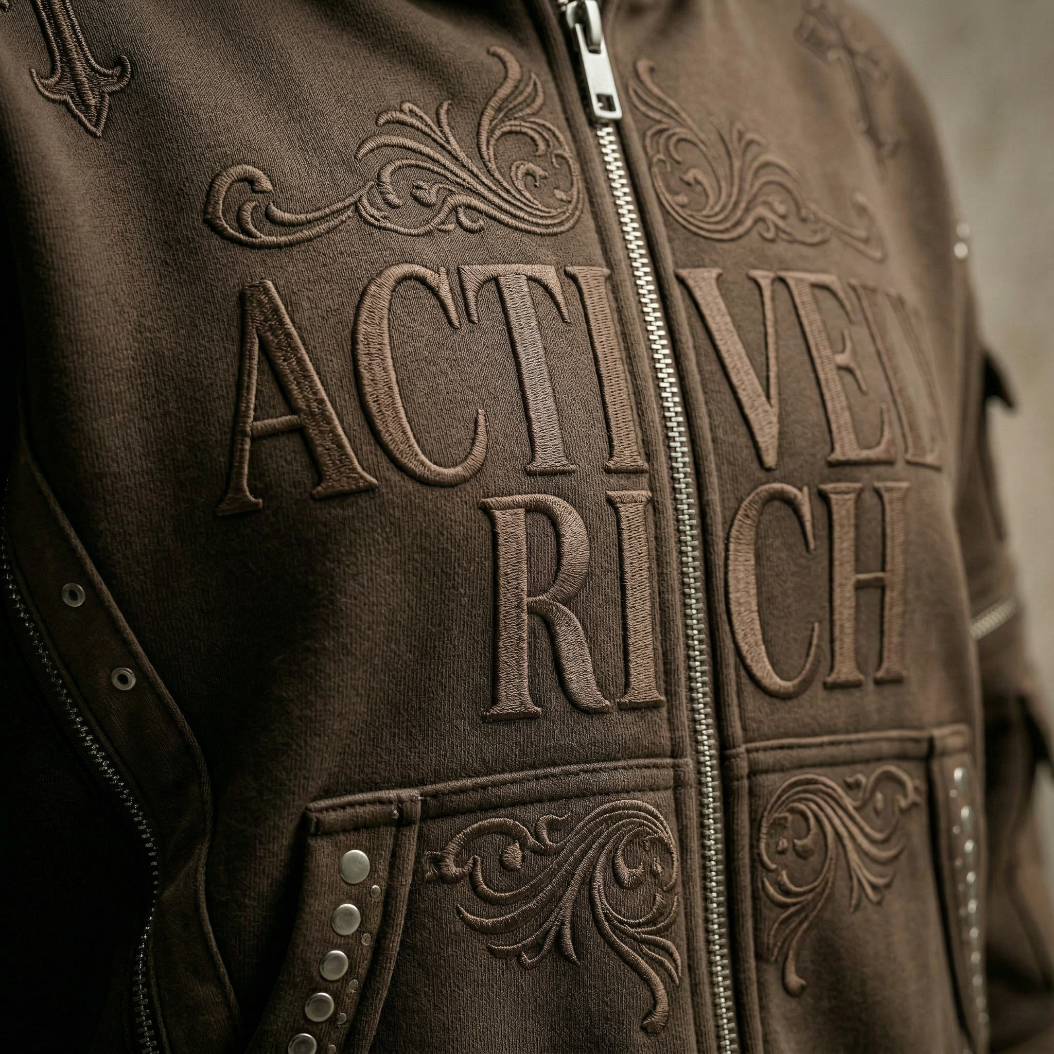 Actively Rich Ascension Noir luxury streetwear hoodie front detail featuring tonal embossed logo, zipper closure, and ornamental stitching in brown